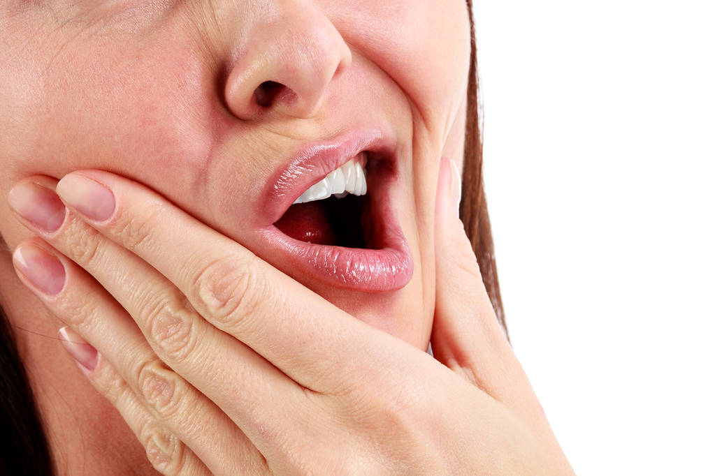 Closeup of woman in strong toothache pain with hands over face.